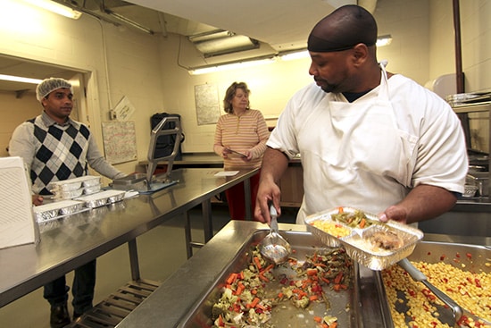 Omari Small, right, and Jubin Jose, left, prepare hot meals for local Meals on Wheels delivery volunteers such as Jessie MacCrae, centre, at the True Davidson Acres nursing home on Dec. 4. PHOTO: Andrew Hudson